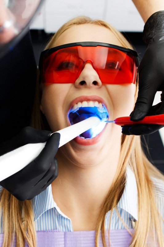 Patient in red glasses sits in a chair at the dentist office while doctor whiten her teeth